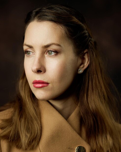 Woman with long brown hair looking downward against a dark background.