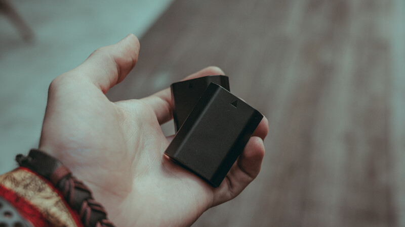 Hand holding a black rectangular device or object against a blurred neutral background.