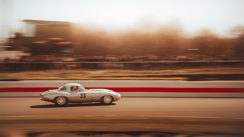 Vintage race car with red and white livery driving on a track with motion blur.