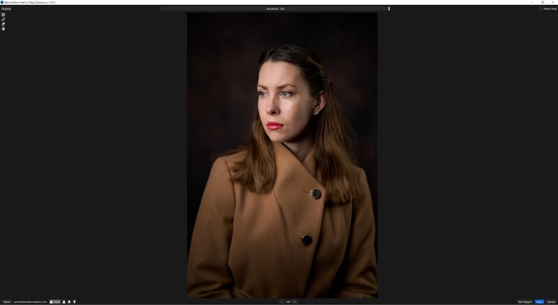 Woman with long brown hair wearing a tan blazer against a dark background.