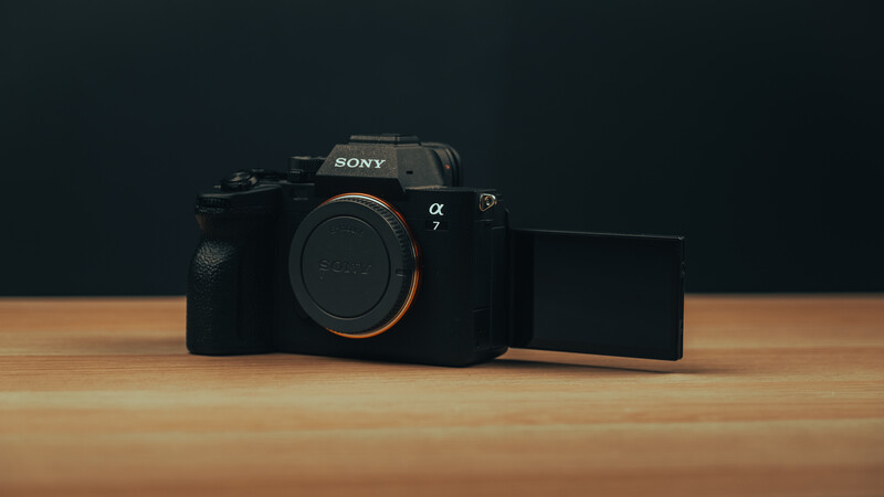 Sony Alpha 7 mirrorless camera body with articulating screen displayed on wooden surface against dark background.
