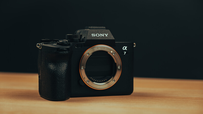 Sony α7 mirrorless camera body with lens mount visible, positioned on wooden surface against dark background.