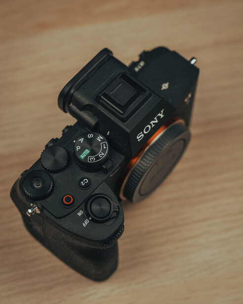 Sony mirrorless camera body shown from above on wooden surface, displaying top controls and mode dial.