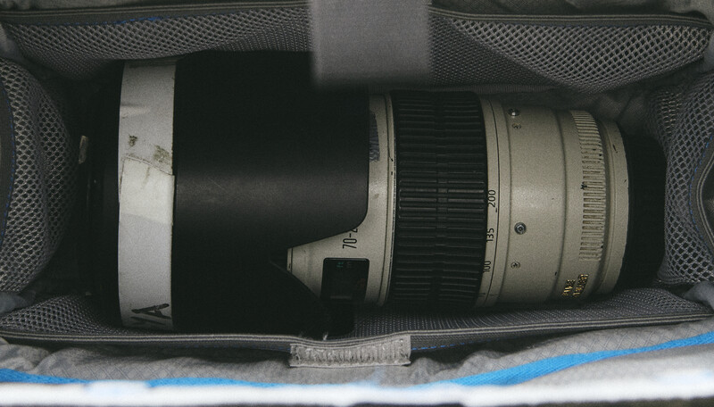 Telephoto lens with white lens hood stored in gray padded camera bag with mesh pockets.