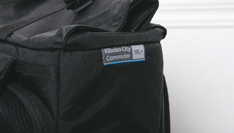 Close-up of a black camera bag with a white label reading "Kiboko City Commuter" and blue accents.
