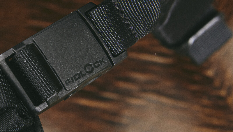 Close-up of a black tactical belt with nylon webbing and a dark metal buckle on a wooden surface.