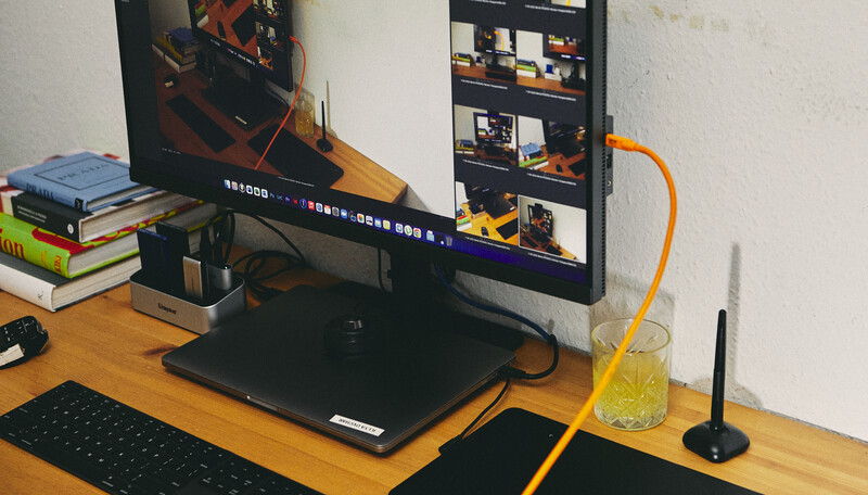 Wooden desk setup with dual monitors, keyboard, and creative workspace surrounded by books and desk accessories.