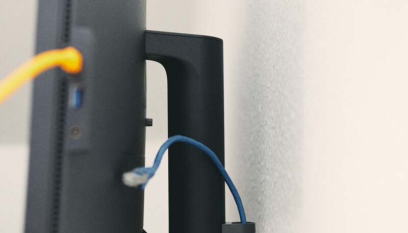 Close-up of yellow and blue cables threaded through a black cable management bracket mounted on a wall.
