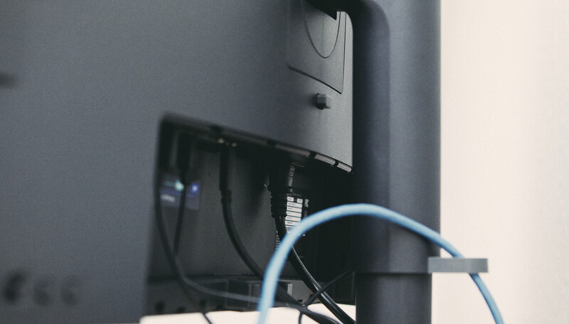 Monitor mounted on a wall with cables and a blue ethernet cord visible behind the display.