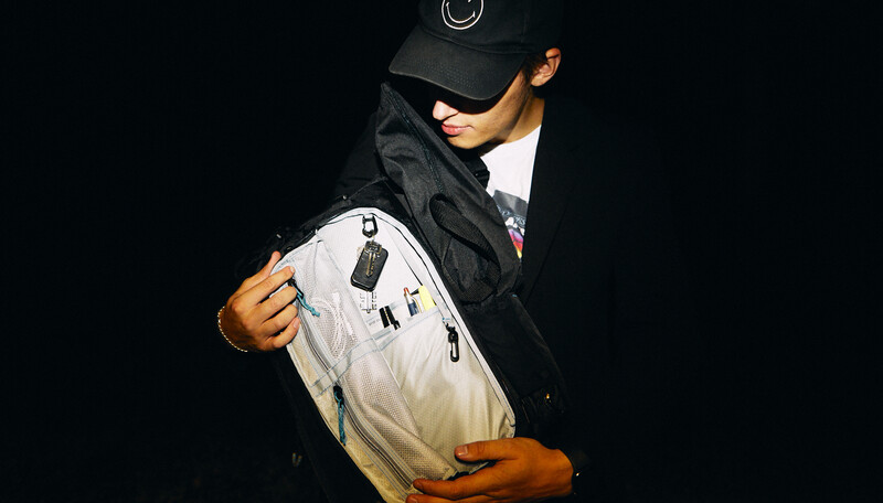 Person in black cap and jacket holding white and cream-colored garment against dark background.