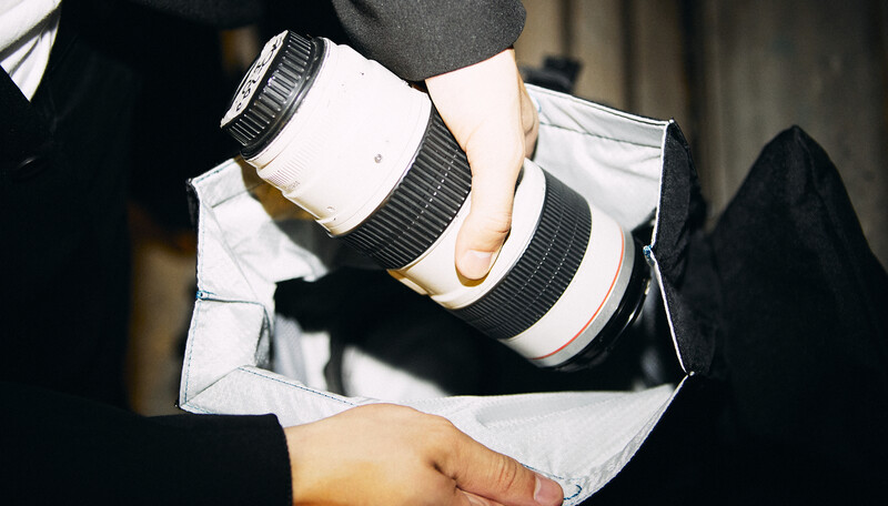 Photographer holding two telephoto lenses wrapped in white lens cases and black grip rings.
