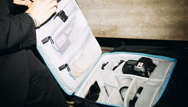 Person opening a packing cube filled with organized camera gear and accessories inside a turquoise-trimmed suitcase.