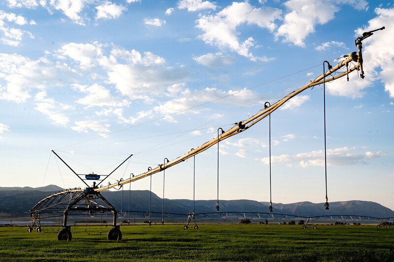 A large center pivot irrigation system extends across a green agricultural field under a partly cloudy sky.