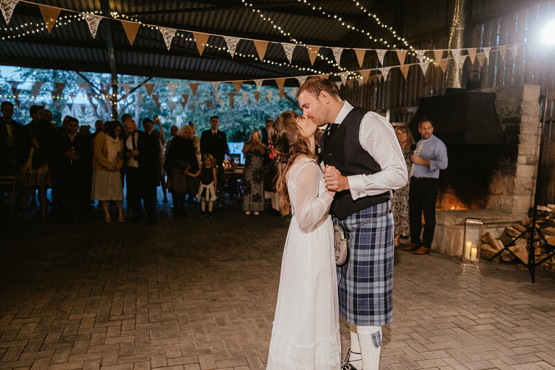 Bride and groom share their first dance under string lights and bunting at an outdoor evening reception.