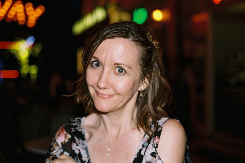 Woman smiling at camera in front of blurred neon signs at night.