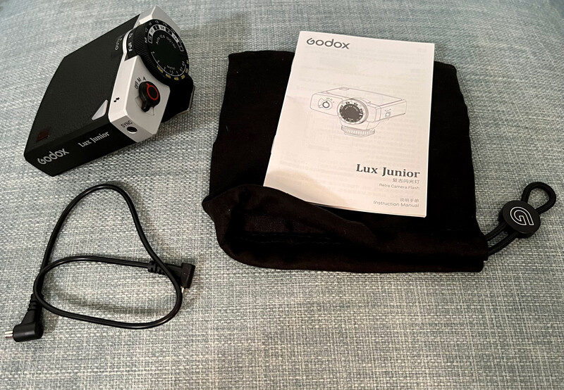 Godox Lux Junior camera flash with manual, cables, and black carrying case arranged on gray fabric.