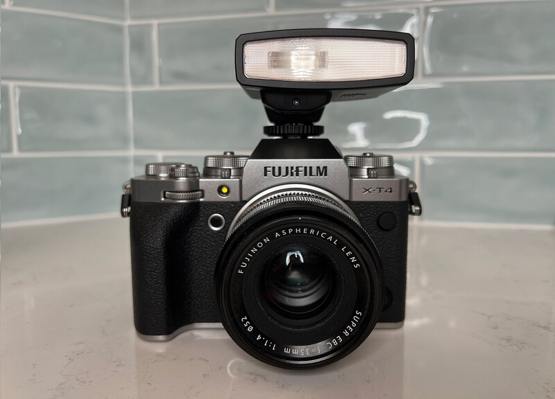 Fujifilm X-T1 camera with external flash mounted on top, displayed against a brick wall backdrop.