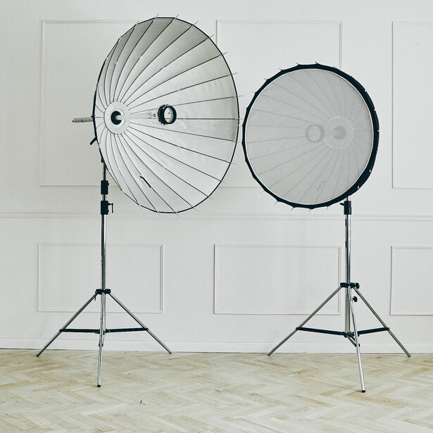 Two photography reflectors on tripod stands against a white wall backdrop.