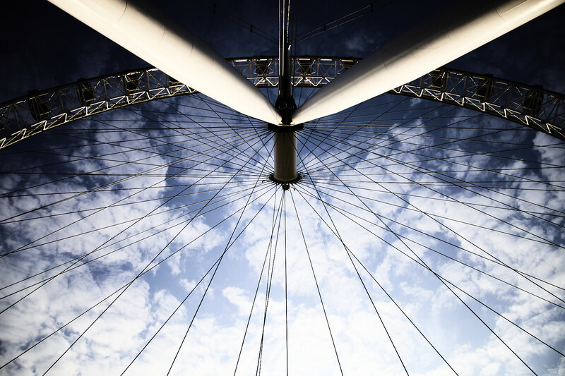 Upward view of a Ferris wheel's metal structure and cables against a cloudy sky.