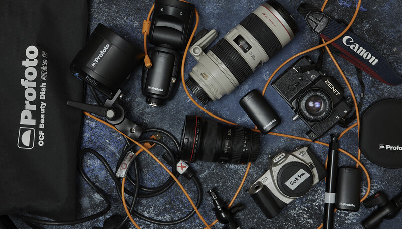 Overhead flat lay of professional photography equipment including cameras, lenses, and lighting gear arranged on a textured surface.