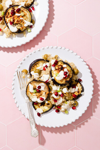 Two plated dishes with roasted zucchini rounds topped with cheese and pomegranate seeds on a pink background.