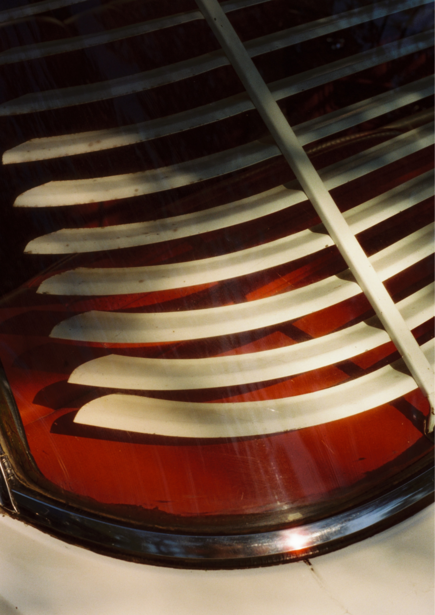 Close-up of a red car taillight with horizontal chrome slats creating geometric patterns and reflections.