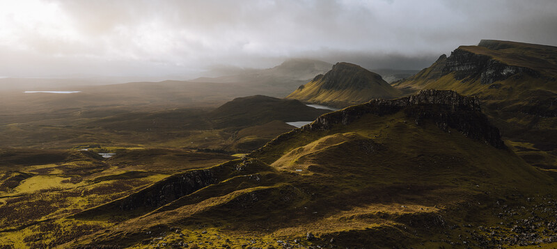 Dramatic volcanic landscape with moss-covered mountains, a tarn, and layered basalt cliffs under stormy light.