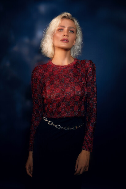 Woman with platinum blonde hair wearing a burgundy sequined long-sleeve top against a dark blue blurred background.