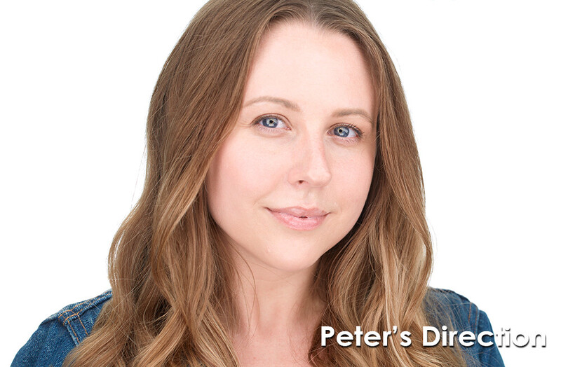 Woman with brown wavy hair and blue eyes wearing denim shirt against white background.