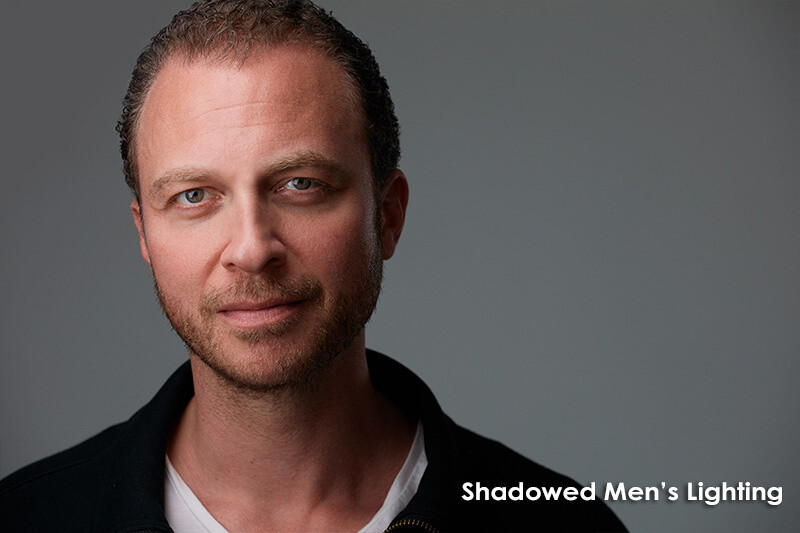 Male portrait with shadowed side lighting against neutral gray background.