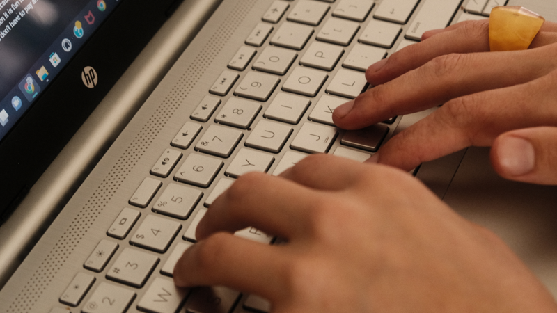 Hands typing on a white keyboard with a laptop screen visible in the frame.