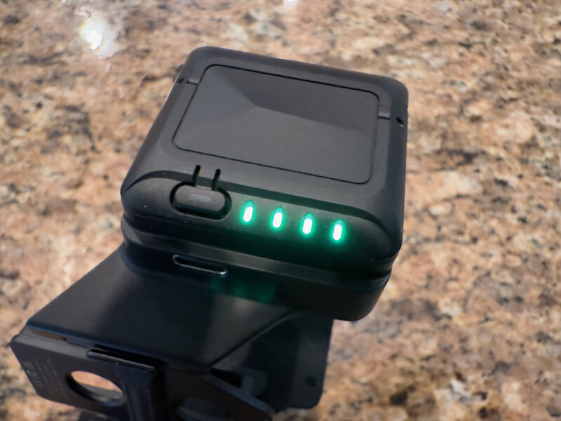 Black compact device with four illuminated green LED indicators mounted on a bracket against a granite surface.