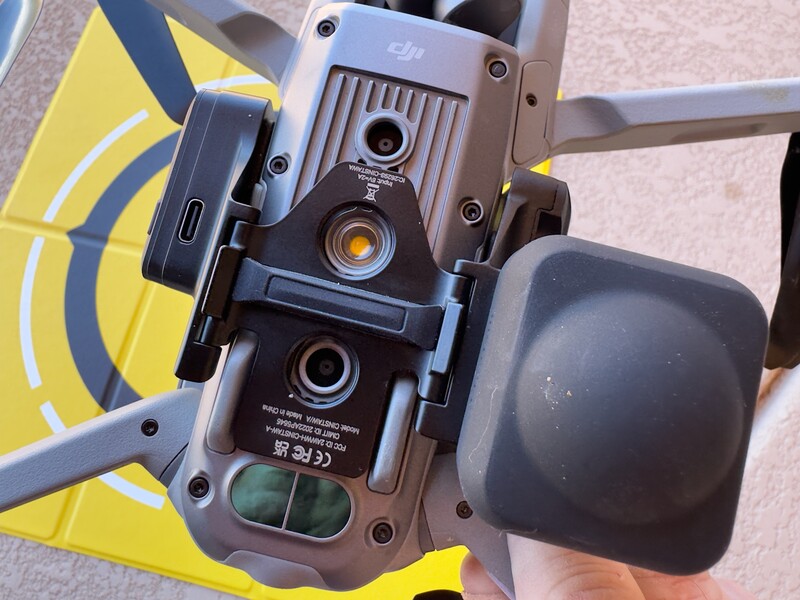Bottom view of a drone showing dual camera modules, battery compartment, and landing gear against yellow propeller.