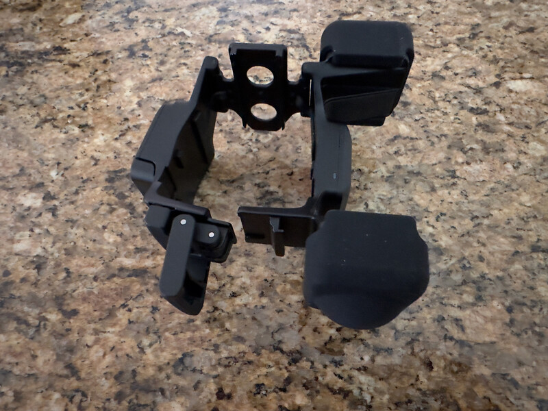 Disassembled black plastic camera flash diffuser components laid flat on granite surface.