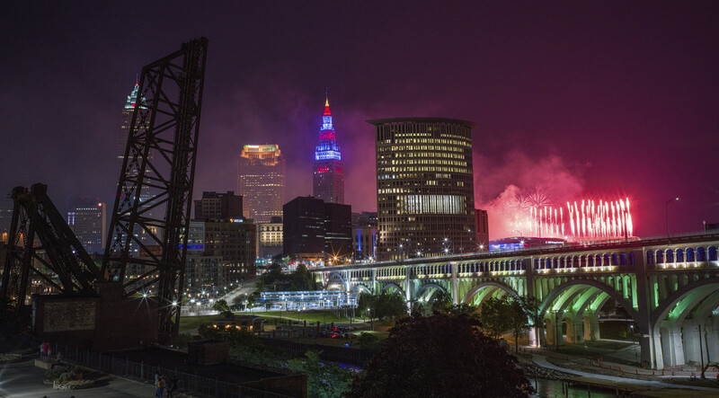 Downtown city skyline at night with illuminated skyscrapers, a steel bridge, and pink-purple sky.