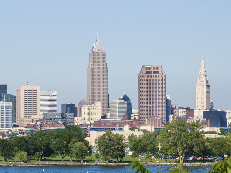 Skyline of a Midwestern city with tall buildings and church spires reflected across a blue river.