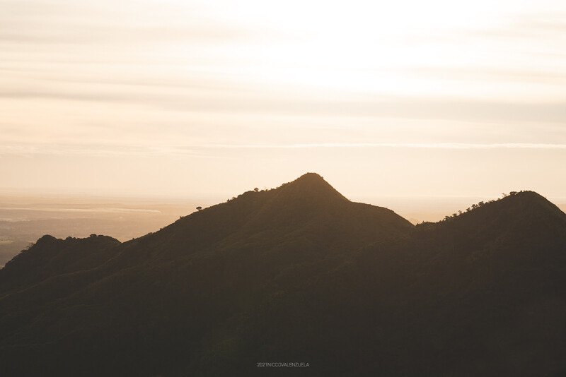 Silhouetted mountain peaks against a hazy golden sky at sunset or sunrise.
