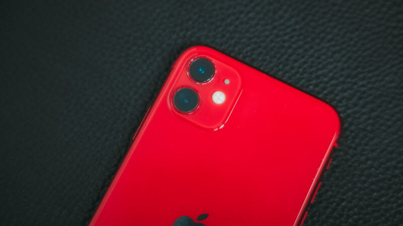 Red smartphone with dual-lens camera system viewed from above on dark textured surface.