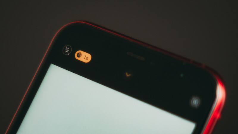Close-up of a smartphone's top bezel showing camera, sensors, and status indicators against dark background.