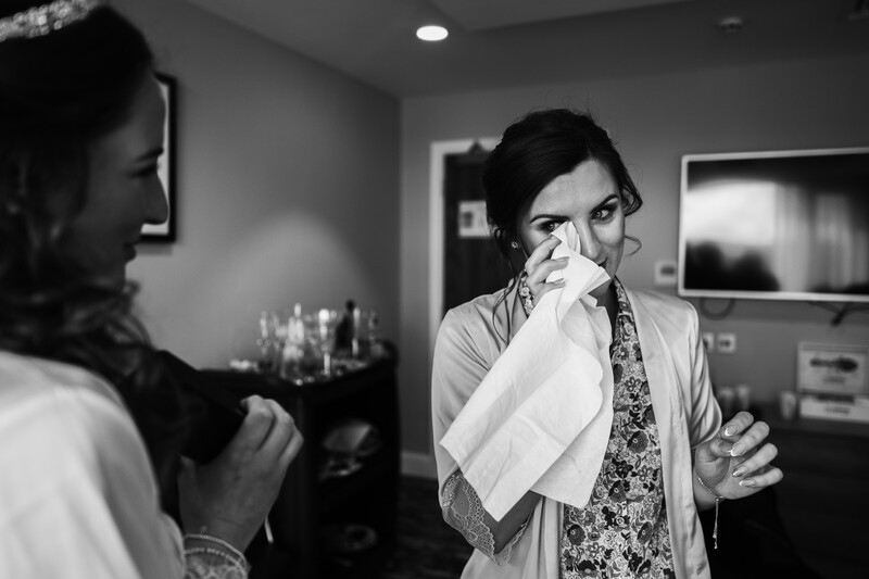 Man in patterned shirt holding tissue to his face while speaking with woman in indoor setting.
