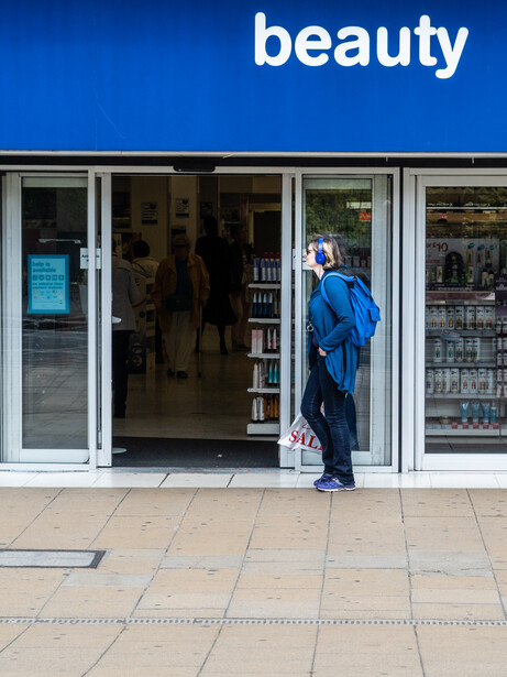 Person in blue jacket entering a storefront with 'beauty' signage above large display windows.