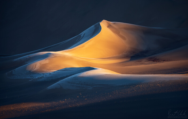 Golden sand dunes with sharp ridges and shadows under dramatic blue and orange lighting.