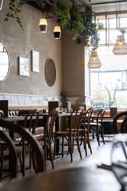 Modern restaurant interior with wooden chairs, concrete wall, and natural window light.