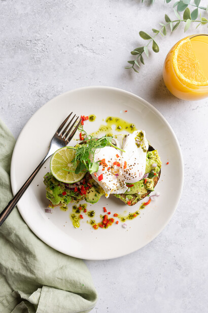 Plated avocado toast with poached egg, microgreens, and colorful garnishes on white dish.