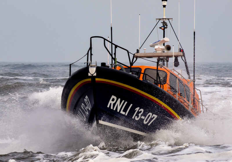 RNLI rescue lifeboat launching through rough surf during active sea conditions.
