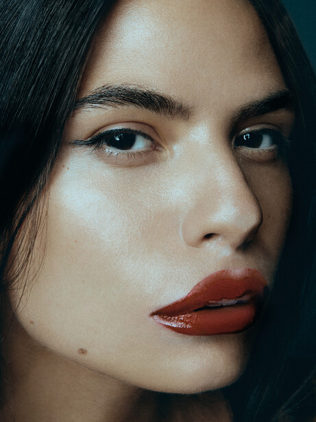 Close-up portrait of woman with dark hair and bold red lips looking directly at camera.