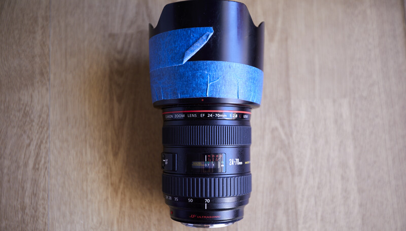Camera lens wrapped in blue painter's tape, displayed vertically against a wooden surface.