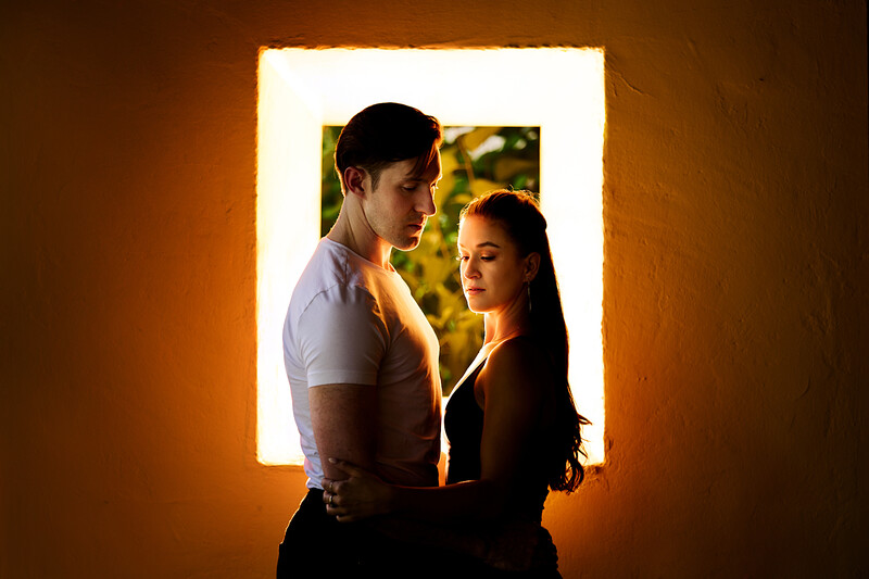 Couple silhouetted against a bright rectangular window backlit with warm golden light.