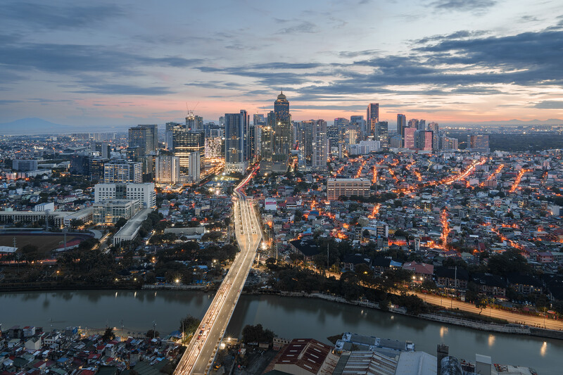 Downtown cityscape at dusk with illuminated skyscrapers, a curved highway, and a river below.
