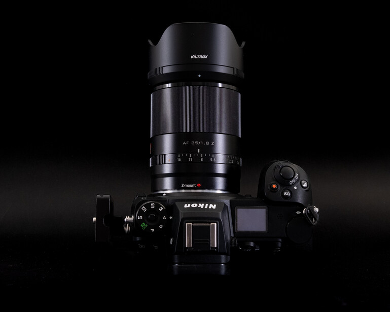 Mirrorless camera with attached telephoto lens and lens hood against black background.